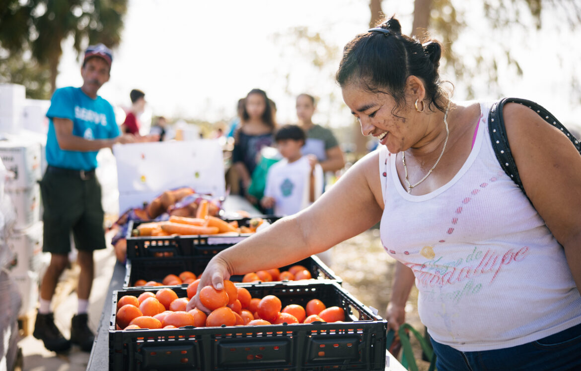 A woman smiles as she selects produce at a food distribution.
